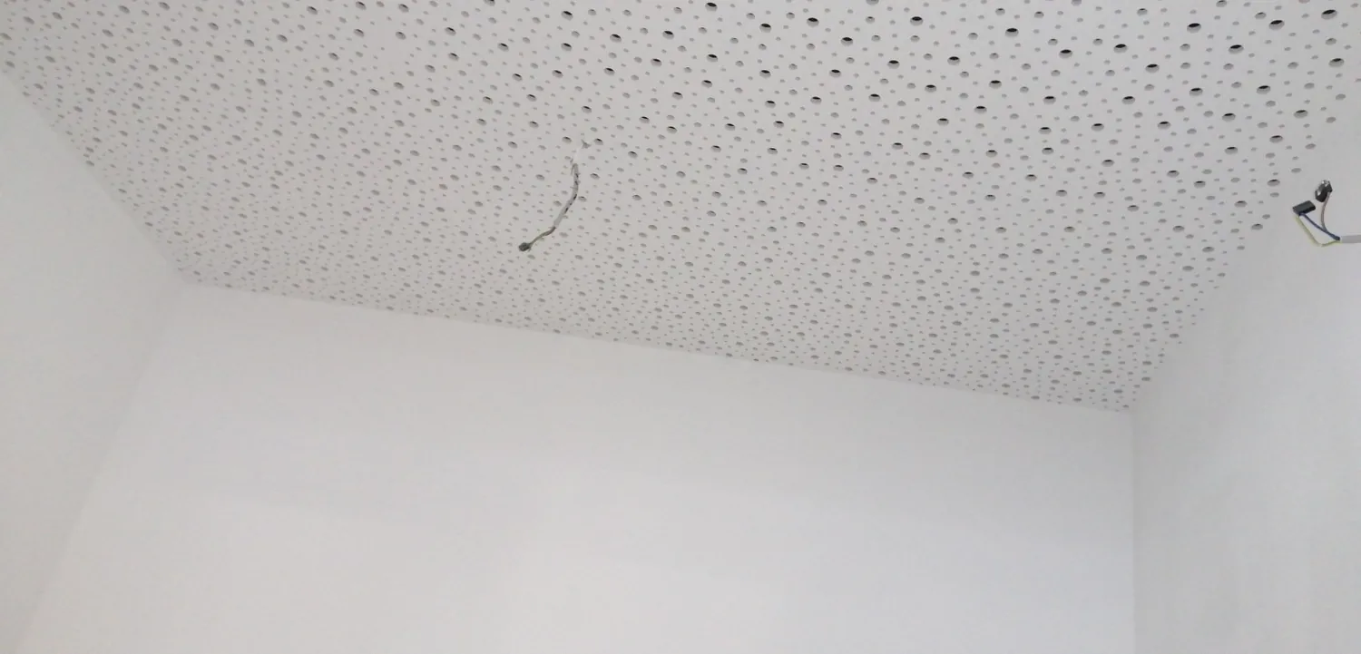 Perforierte weiße Akustikplatten an einer Decke mit offenen Leitungen